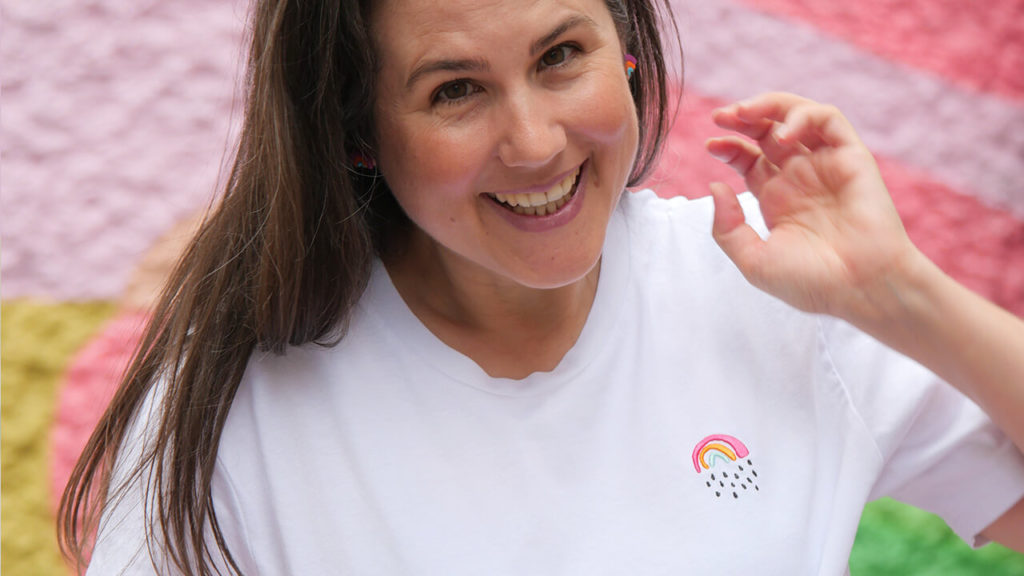 Sarah trägt ein weißes t-Shirt mit einem kleinen Regenbogen-Stick