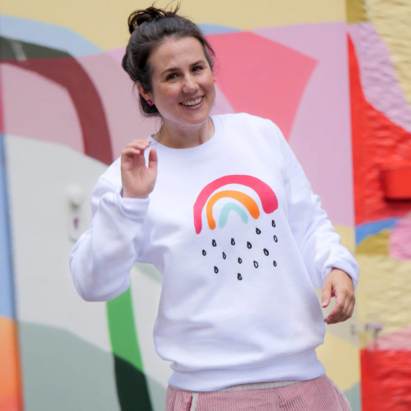 Sarah trägt einen Pulli aus der Kleinen Regenbogen Kollektion