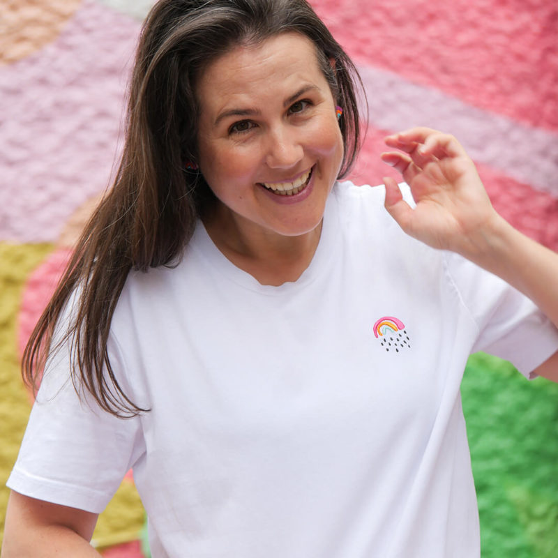 Sarah trägt ein weißes T-Shirt mit einem kleinen Regenbogen Stick