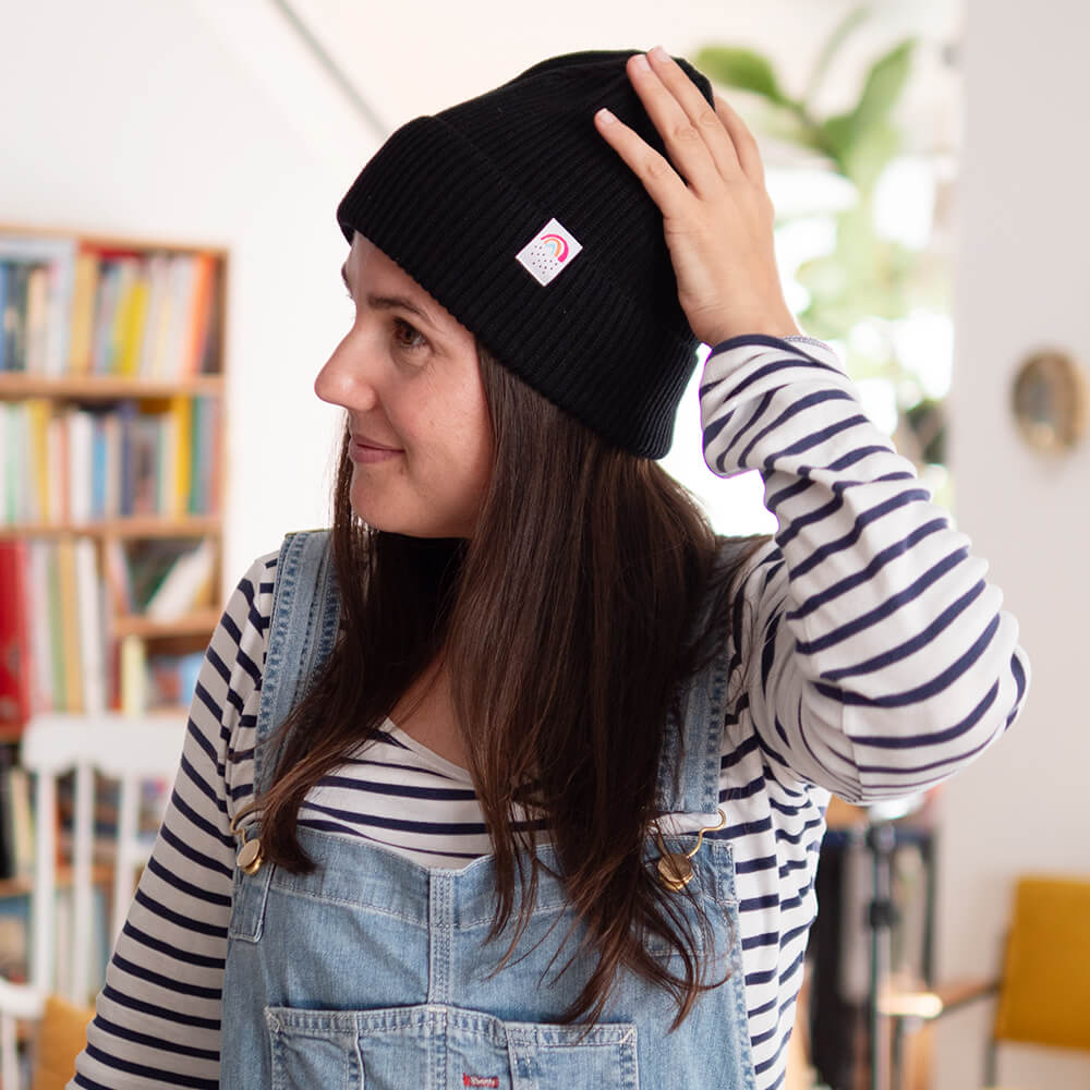 Sarah Gilgien trägt eine schwarze Fisherman Beanie mit einem kleinen Regenbogen Webetikett an der Seite