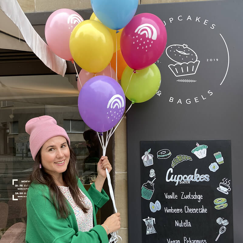 Sarah Gilgien mit bunten Luftballons wo ihre Illustration Kleine Regenbogen zu sehen ist